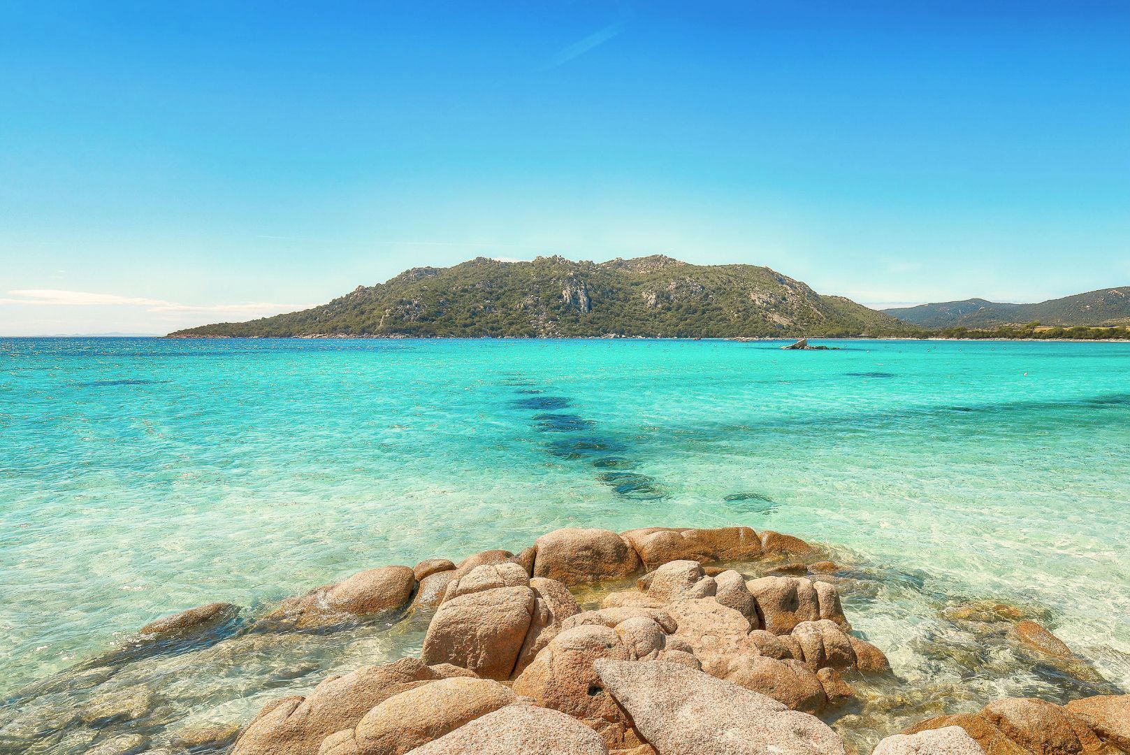Plage de Porto-Vecchio avec rochers et eau transparente face aux collines