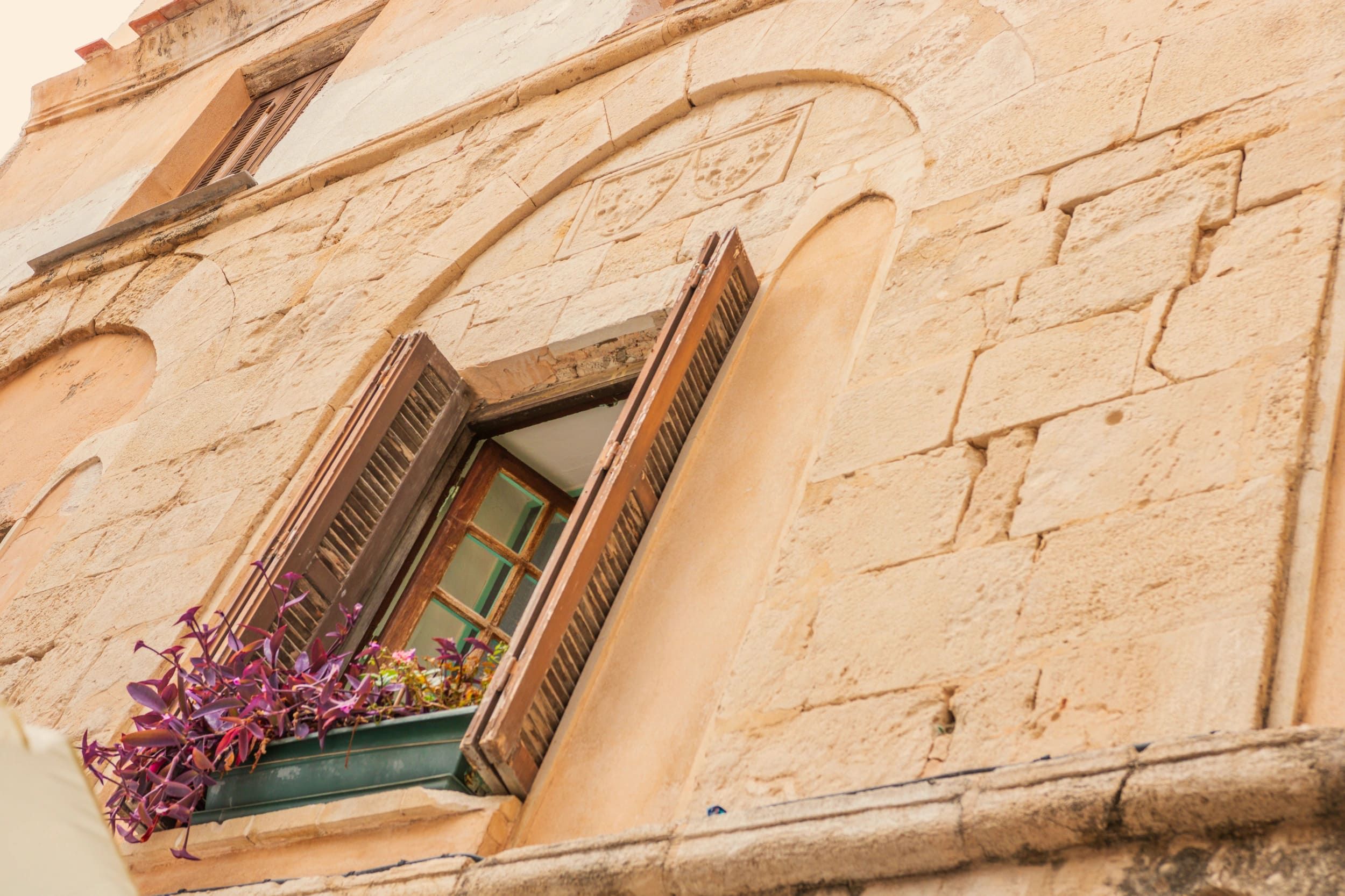 Façade en pierre d’un bâtiment ancien avec fenêtre et bouquet de fleurs