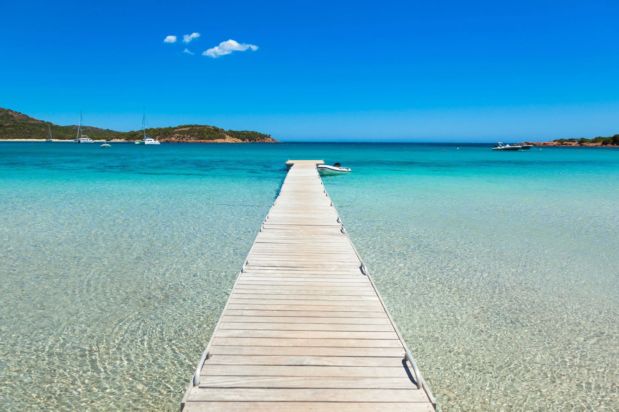 Ponton en bois menant à une eau turquoise dans une baie du sud de la Corse